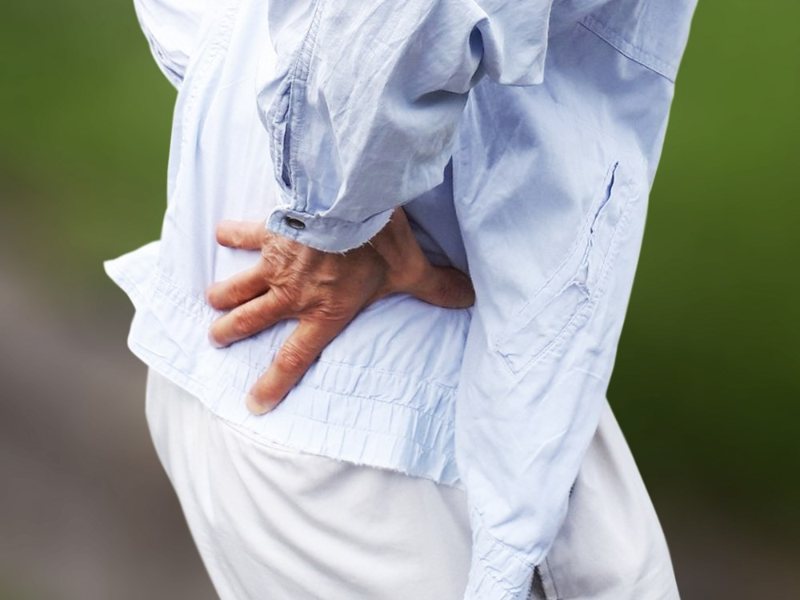An older person with a hand pressed to their lower back
