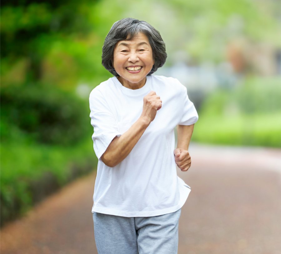 A smiling older woman jogging in a green park