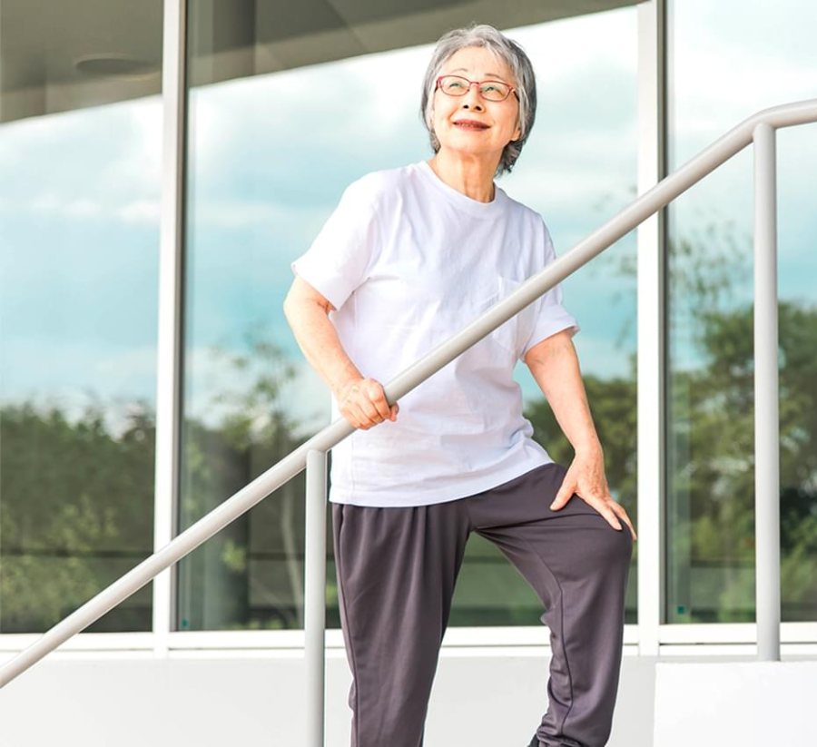 An older woman with glasses climbing steps beside a handrail, one hand on her knee